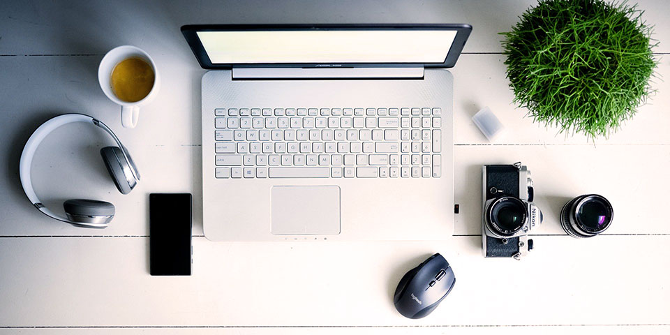 Schreibtisch von oben mit Laptop, Kamera, Kopfhörern und Smartphone